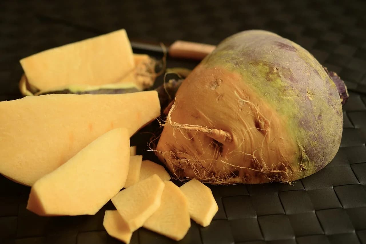 Rutabaga whole and cut into yellow slices on a dark woven surface with a knife in the background