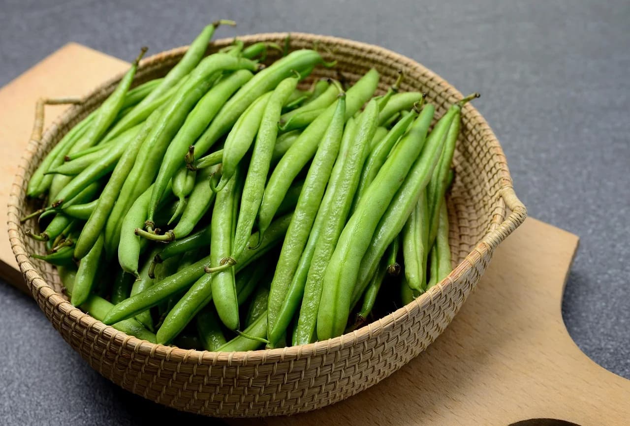 Bush bean fresh green pods with stems in a woven basket on a wooden board