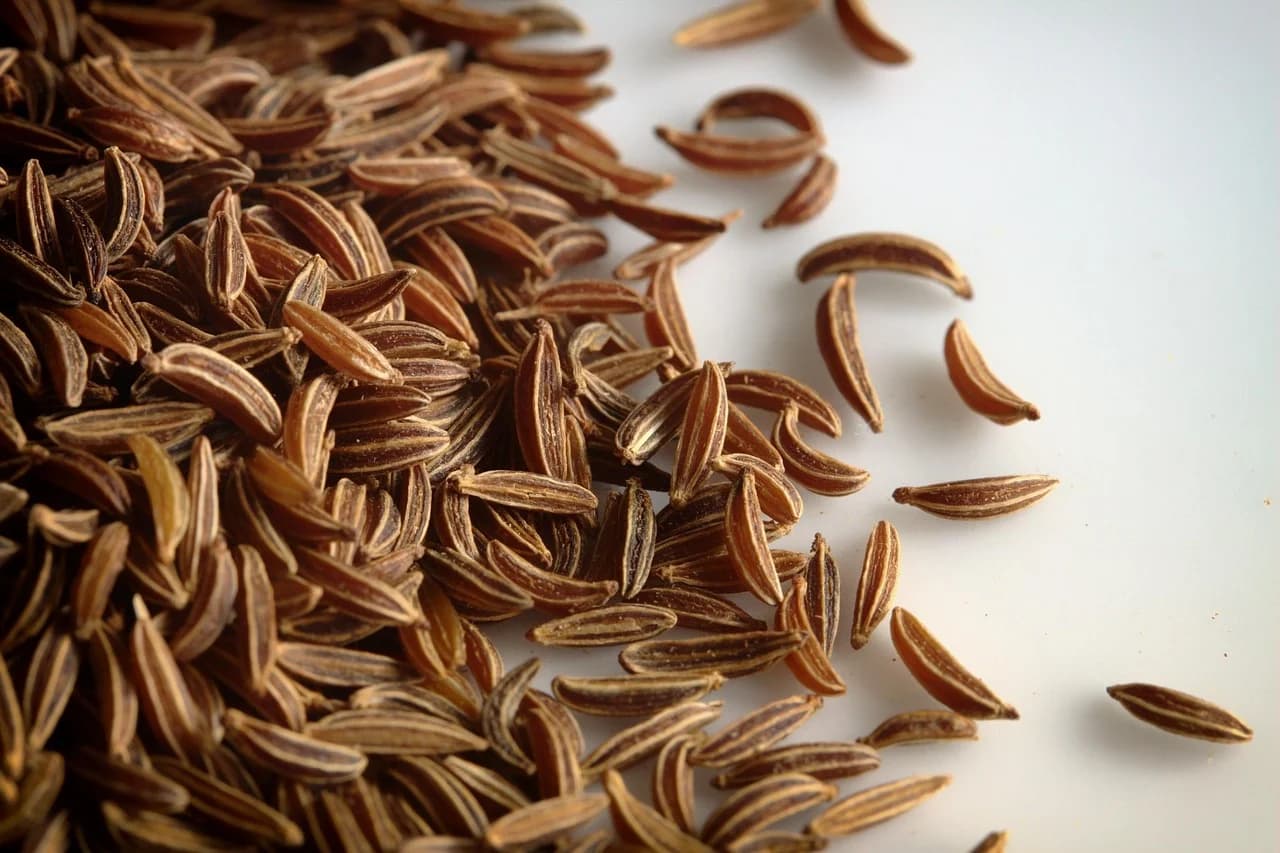 Close-up of dried brown crescent-shaped caraway seeds scattered on a white surface