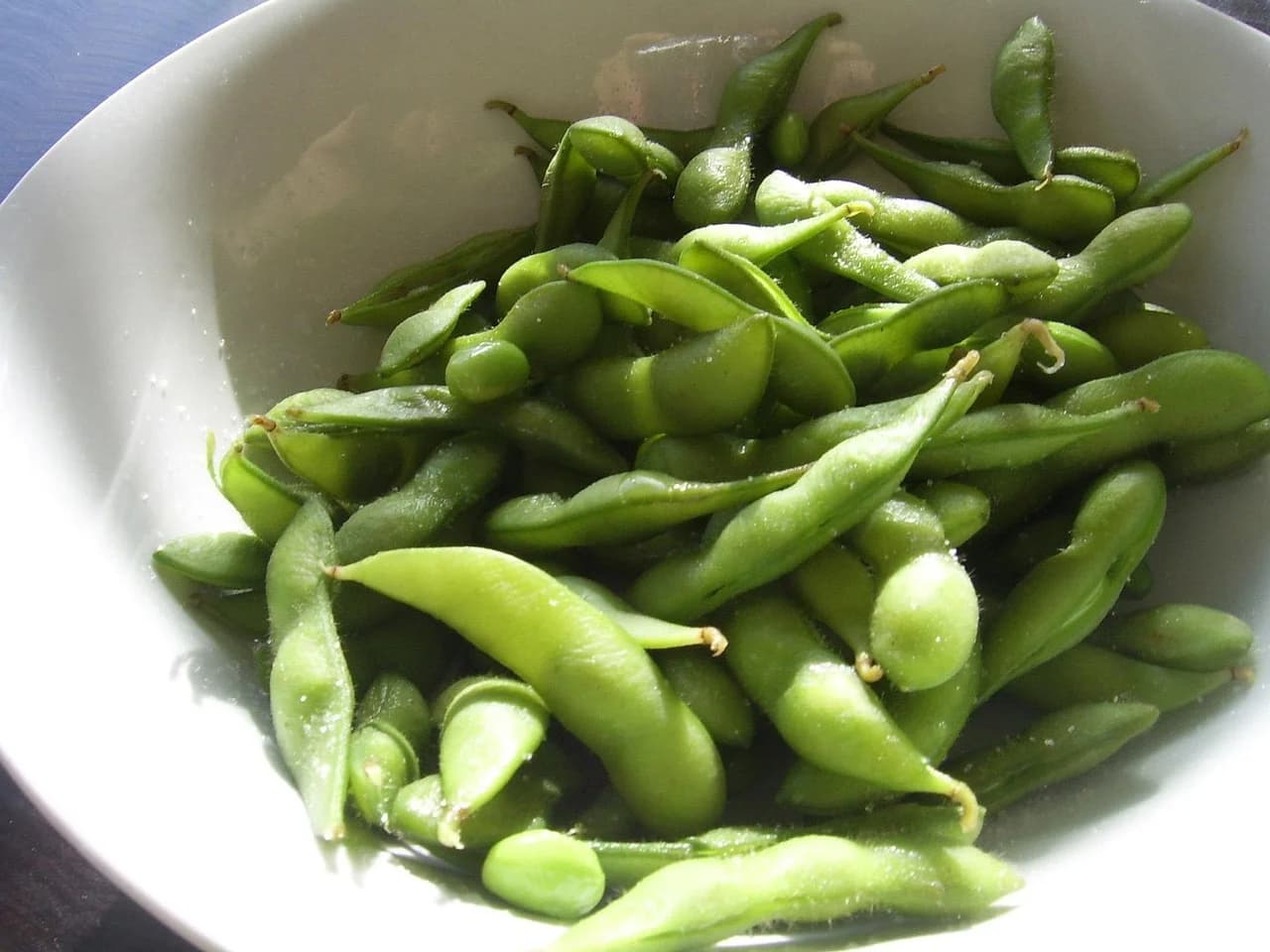 Edamame pods in a white bowl with sunlight falling across them